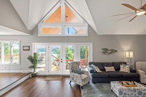 A spacious living room with a high ceiling, a ceiling fan, a large window, and a view of a deck.