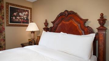 A neatly made bed with a wooden headboard, a bedside lamp, and a framed floral painting on the wall.