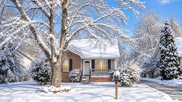A residential house with a brick exterior, a front porch, and snow-covered trees.