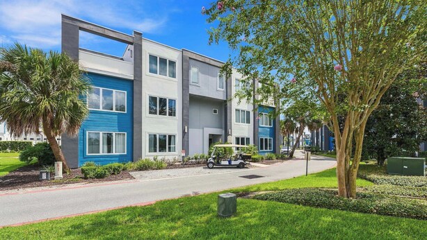A modern multi-story residential building with a flat roof, large windows, and a well-maintained lawn.