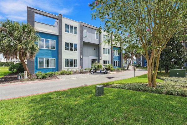 A modern multi-story residential building with a flat roof, large windows, and a well-maintained lawn.