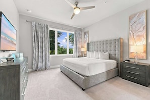 A bedroom with a bed, nightstands, a desk, a ceiling fan, and a window with curtains.