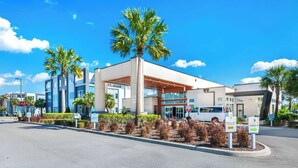 A modern hotel with a covered entrance, palm trees, and a clear blue sky.