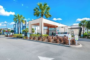 A modern hotel with a covered entrance, palm trees, and a clear blue sky.