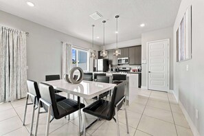 A modern kitchen with stainless steel appliances, a dining area with a white table and black chairs, and pendant lighting. - Beautiful Condo near Disney with Resort & Waterpark Access - B23-109 (Kissimmee)