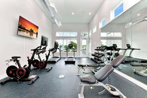 Ein Fitnessraum mit Trainingsgeräten, einem großen Spiegel und einem Sonnenuntergangsbild.