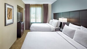 Ein Hotelzimmer mit zwei Betten, einem Fernseher, einer Lampe und einem gerahmten Bild an der Wand.