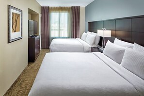 Hotellihuone, jossa on kaksi sänkyä, televisio, lamppu ja seinällä oleva kehystetty kuva.
