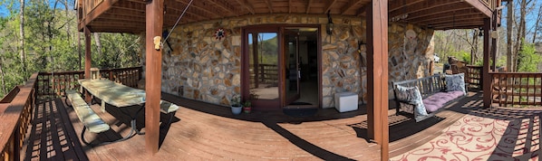 A wooden deck with a stone wall, a covered seating area, and a door leading inside.