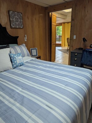Een slaapkamer met een bed, een nachtkastje met een lamp, een ingelijst certificaat en uitzicht op een buitengebied.