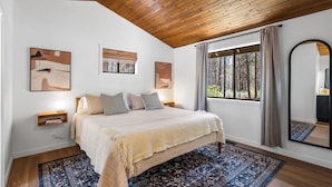 A bedroom with a large bed, a window with a view of trees, and a wooden ceiling. - Cozy 3 bedroom house near Sunriver, 20 minutes to Mt.Bachelor.Hot tub Pool Table (Bend)