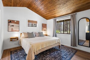 A bedroom with a large bed, a window with a view of trees, and a wooden ceiling. - Cozy 3 bedroom house near Sunriver, 20 minutes to Mt.Bachelor.Hot tub Pool Table (Bend)