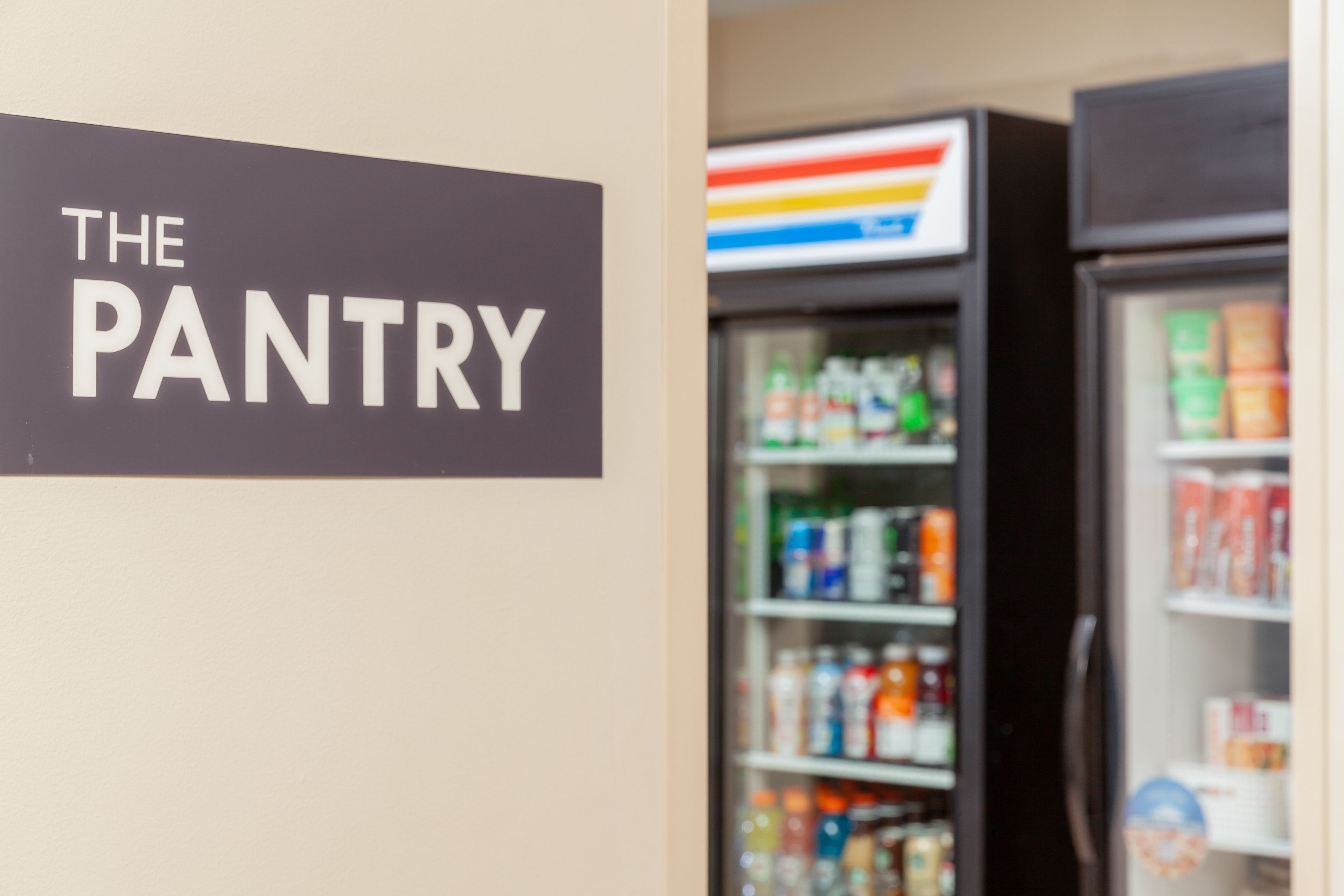 Kyltti, jossa lukee ”THE PANTRY”, ja epätarkka kuva jääkaapilla varustetusta tuotehyllystä, jossa on erilaisia tuotteita.