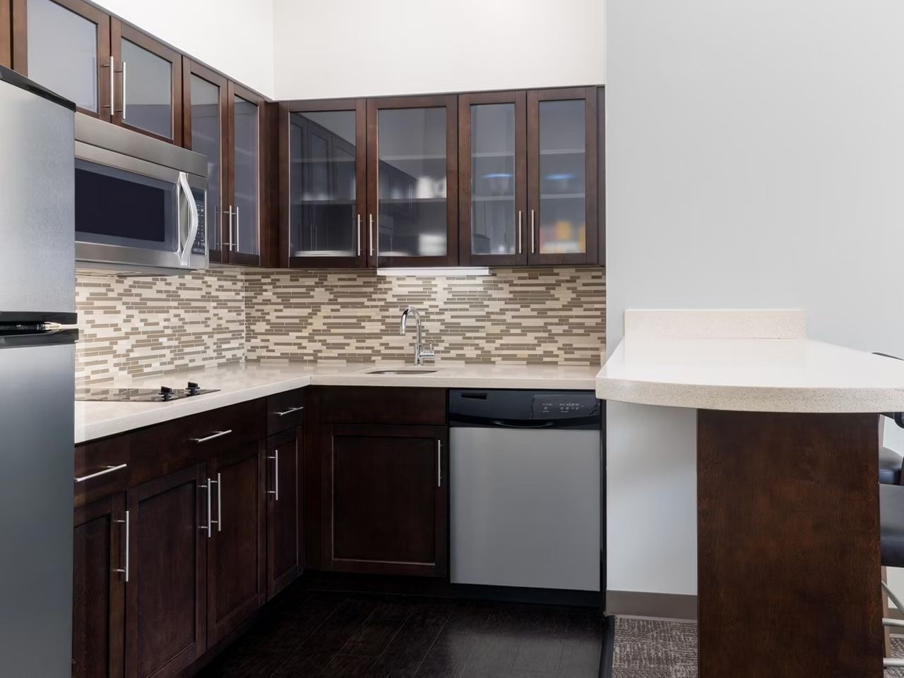 A modern kitchen with dark wood cabinets, a microwave, a dishwasher, and a tiled backsplash.