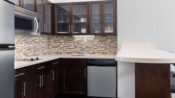 A modern kitchen with dark wood cabinets, a microwave, a dishwasher, and a tiled backsplash.