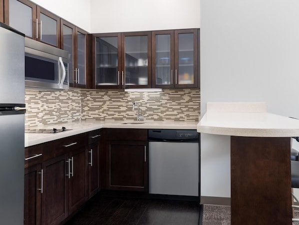 A modern kitchen with dark wood cabinets, a microwave, a dishwasher, and a tiled backsplash.