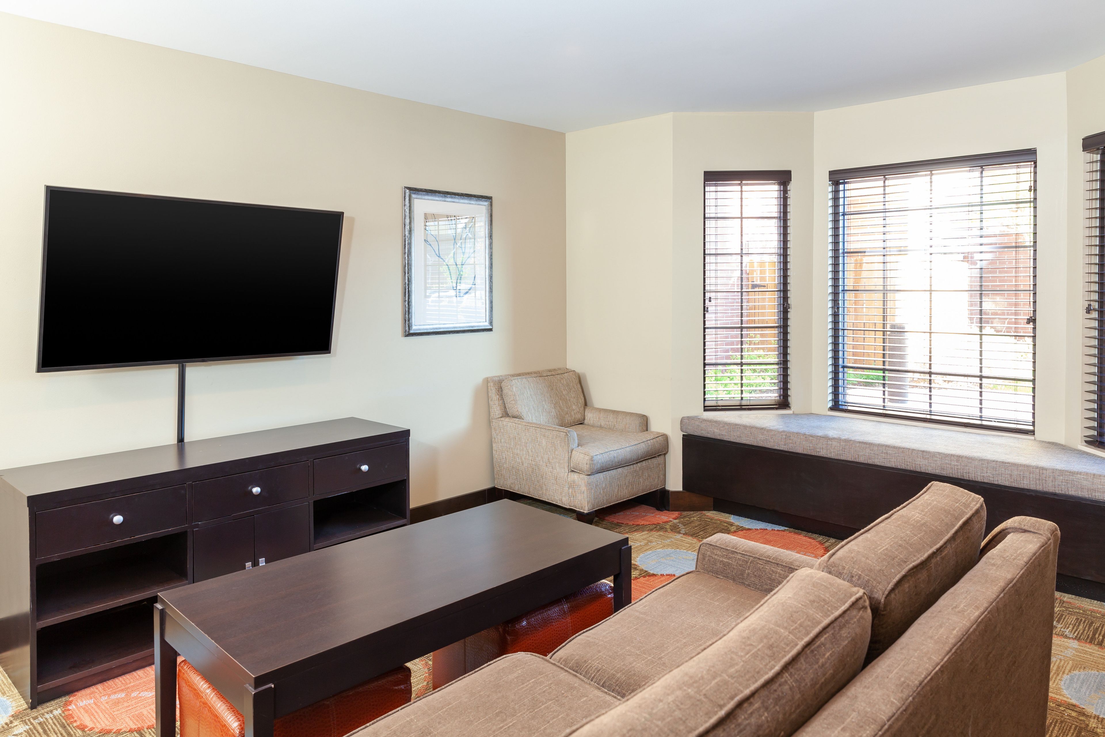 A living room with a flat-screen TV, a sofa, a chair, and a window with blinds.