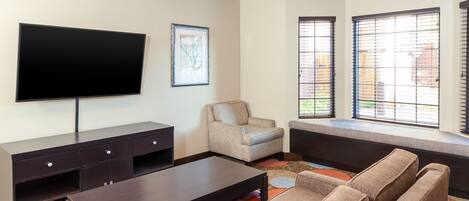A living room with a flat-screen TV, a sofa, a chair, and a window with blinds.
