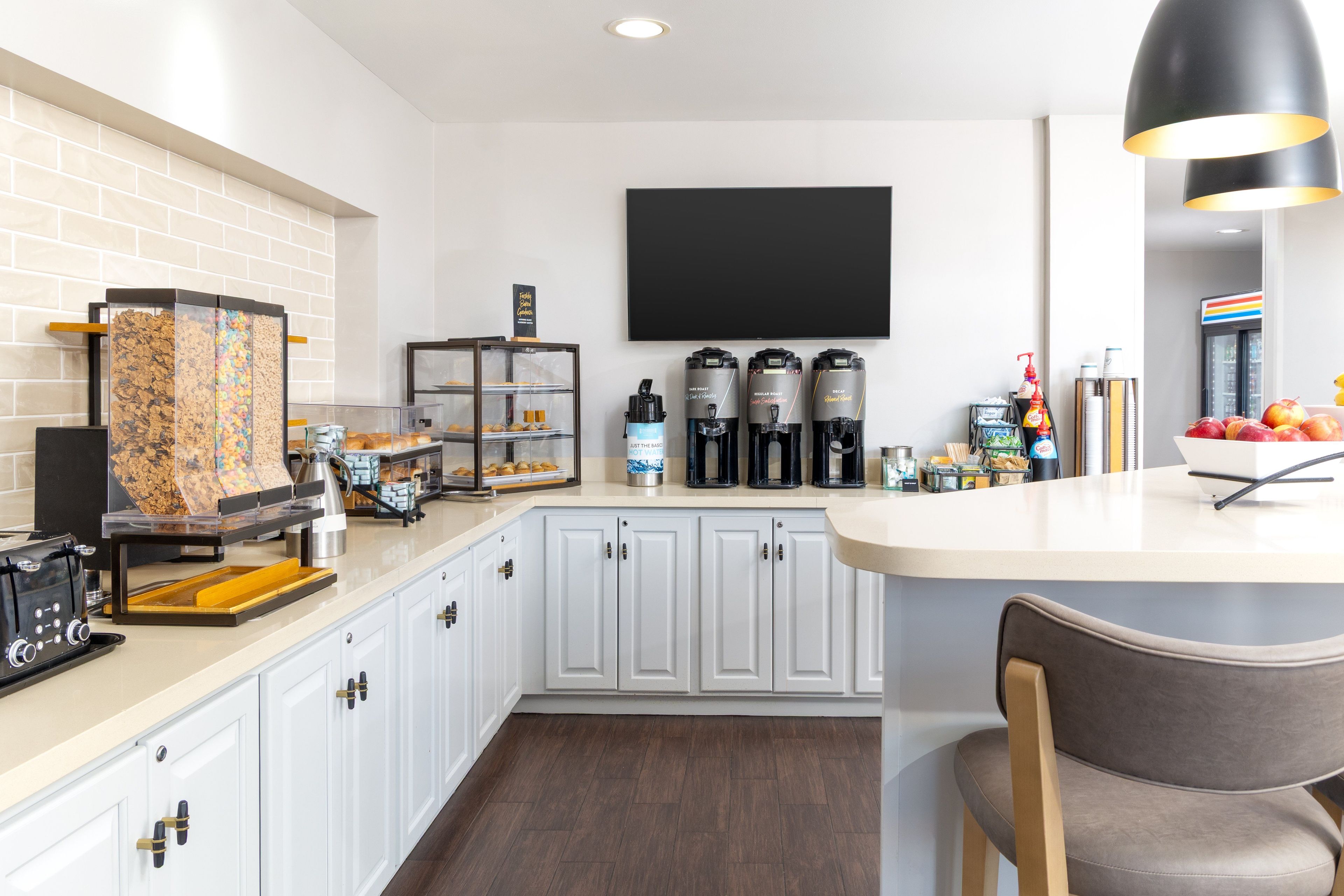 A modern kitchen with a coffee station, a bread display, and a flat-screen TV mounted on the wall.