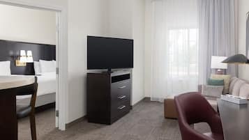 Ein Hotelzimmer mit Bett, Fernseher auf einem Tisch, Schreibtisch mit Stuhl und einem Fenster mit Vorhängen.