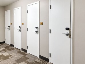 A row of white doors with numbered plaques, a patterned carpet, and a plain wall.