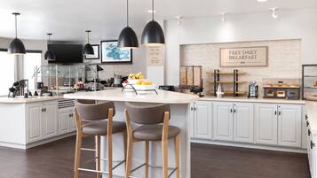 A modern kitchen with a central island, bar stools, pendant lighting, and a breakfast sign.