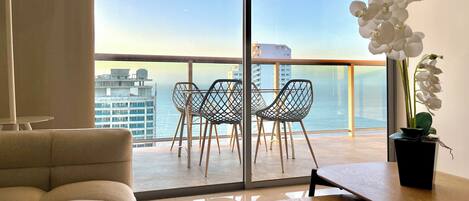 A balcony with a view of the ocean, a sofa, a dining table, and a potted orchid.