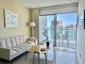 A modern living room with a sofa, a table, a lamp, and a view of the city through large windows. - by Calamari.Homes - Infinitum 3302 - Bocagrande (Bocagrande)