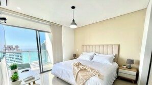 A modern hotel room with a large bed, bedside tables, a desk with a chair, and a view of the city. - by Calamari.Homes - Infinitum 3302 - Bocagrande (Bocagrande)