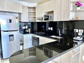 A modern kitchen with a stainless steel refrigerator, a built-in microwave, a gas stove, and a black countertop. - by Calamari.Homes - Infinitum 3302 - Bocagrande (Bocagrande)