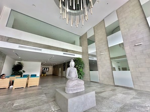 A modern lobby with a Buddha statue, seating area, and a reception desk. - by Calamari.Homes - Infinitum 3302 - Bocagrande (Bocagrande)