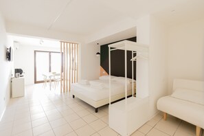 A modern bedroom with a white four-poster bed, a white sofa, and a dining area with a table and chairs. - Visitsicilia Vasile 9 (Castellammare del Golfo)