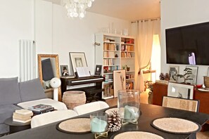 A living room with a piano, bookshelves, a television, and a dining area with a table set for two. - Luxury at the foot of the Eiffel!! (Paris)