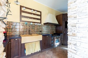A kitchen with a tiled backsplash, wooden cabinets, a stove, and a hanging light fixture. - Visitsicilia Sabbia Dorata (ora n. 497) (Alcamo Marina)