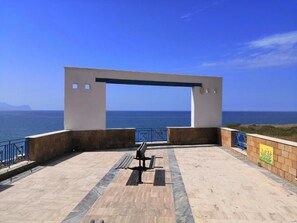 Ein Sitzbereich im Freien mit einer Bank, einer weißen Struktur und Blick aufs Meer.