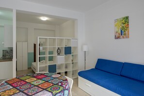 Quarto com cama, sofá azul, guarda-roupa branco e um quadro na parede.
