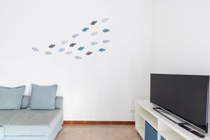 Ein Wohnzimmer mit einer Couch, einem Flachbildfernseher und einer Wandsticker mit Fischen.