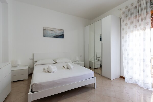 Ein schlicht eingerichtetes Schlafzimmer mit Bett, Nachttischen, einem Spiegel und einem Gemälde an der Wand.