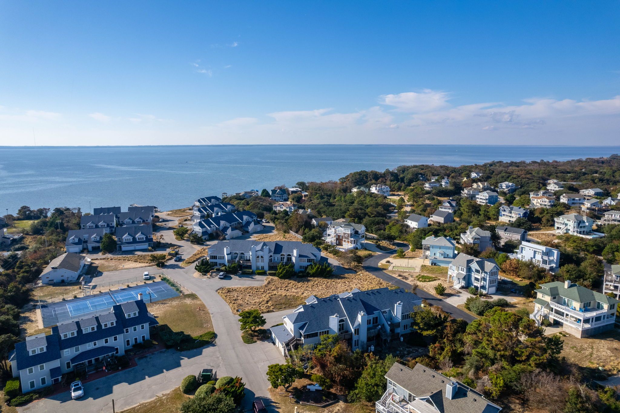 A coastal residential area with houses, a parking lot, and a view of the sea.