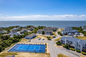 A residential area with houses, a tennis court, and a body of water in the background. - Duck Soundside Retreat King Beds, Pool, Sound Views & Great Amenities! (Kitty Hawk)