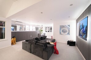 A modern living room with a sectional sofa, a flat-screen TV, and a dining area with a table and chairs. - 3 bed Luxury Home With hot Tub, Free Parking and EV (Northwood)