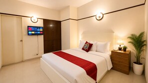 Habitación de hotel con cama, mesita de noche, lámpara y televisor montado en la pared.