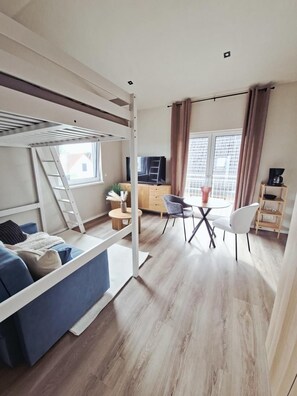 A modern living space with a bunk bed, a dining area with a table and chairs, a TV, and a kitchen area. - NEW! Apartment at the Achim Golf Course (Achim)