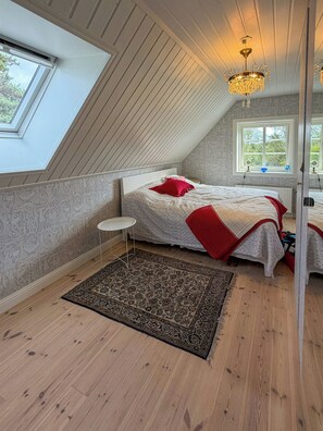 Ein Schlafzimmer mit Schrägdecke, einer Chandelierleuchtreiter, einem Bett mit roten Kissen, einem kleinen runden Tisch und einem gemusterten Teppich.
