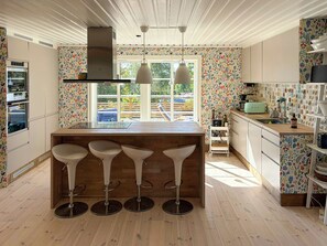 Et moderne køkken med en central ø, barstole, et vindue med udsigt og et mønstret backsplash.
