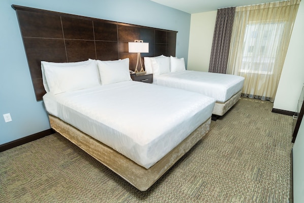 A hotel room with two beds, a dark headboard, a nightstand with a lamp, and a window with curtains.