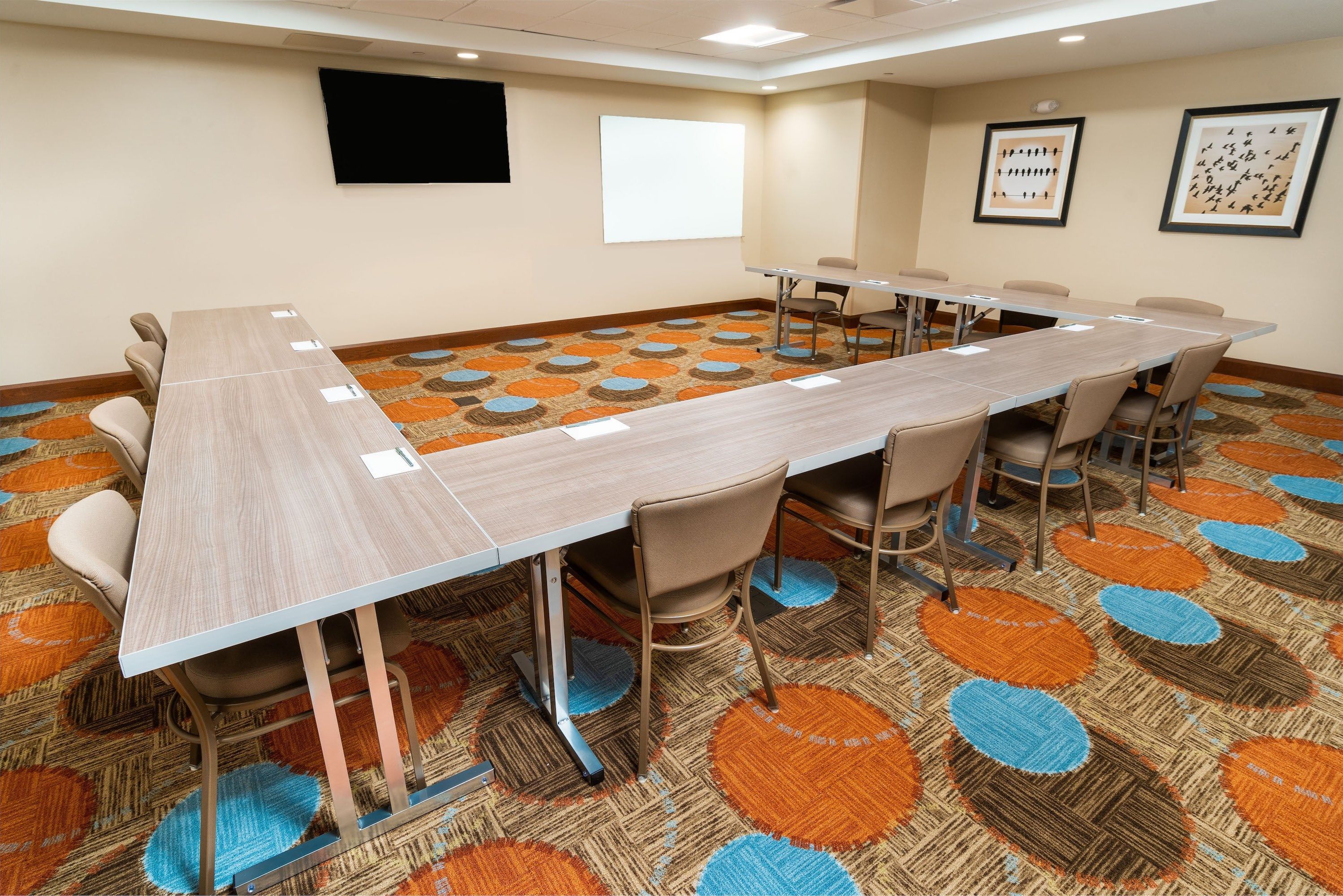A conference room with a long table, chairs, a projector screen, and a carpeted floor.