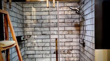 Una doccia con una scala in legno, asciugamani, un soffione metallico e un muro rivestito di piastrelle.
