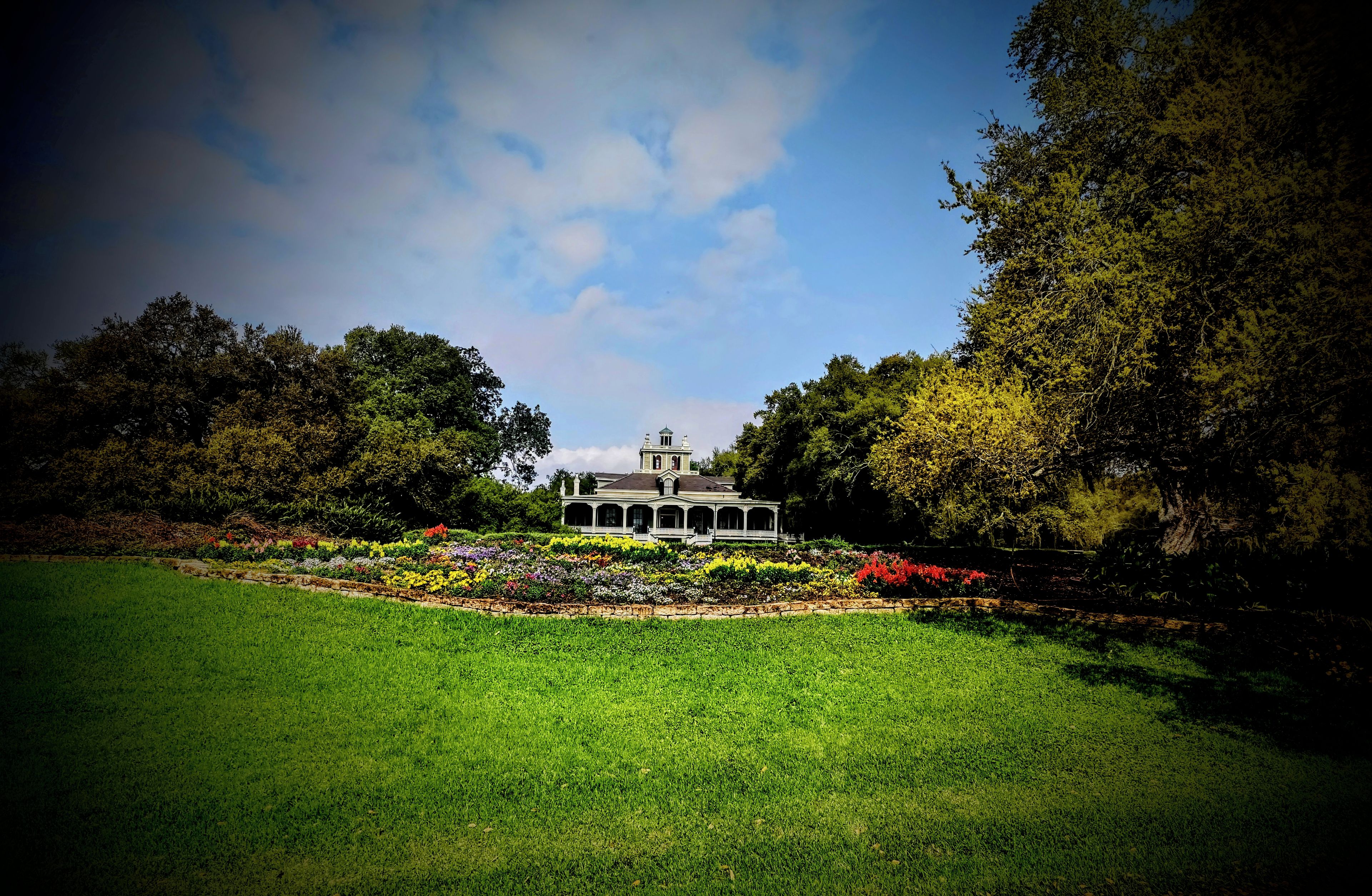 A large, two-story building with a central pavilion, surrounded by a well-maintained garden with various flowering plants.
