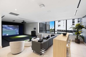 Ein modernes Wohnzimmer mit einem großen Bildschirm, einem Sofa, einem Esstisch und einer Zimmerpflanze.